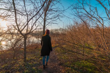 Genç kız gölün kıyısında küçük bir patikada yürüyüş yapıyor.