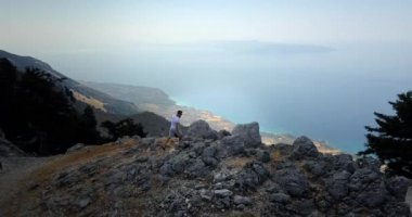 Genç adam büyüleyici manzarayla Kefalonia adasının tepesine tırmanıyor.