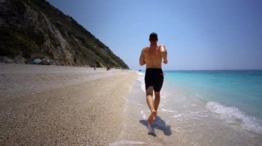 Yunanistan 'ın Lefkada kentindeki güzel kumlu plaj boyunca koşan genç adam Megali Petra