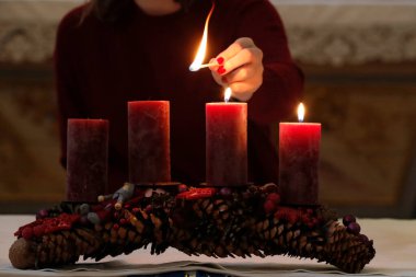 Advent wreath with red candles. Woman lights third candle.  France.  clipart