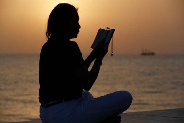 Gün batımında İncil okuyan sadık bir kadının silueti. Din, inanç, dua ve maneviyat kavramı.