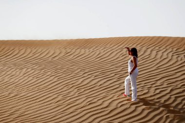 Kadın ayak izleri bırakıyor ve çöl kum tepesine çıkıyor. Birleşik Arap Emirlikleri.