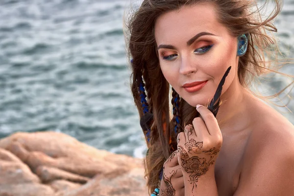 Hermosa chica cerca del mar, accesorios brillantes, mehendi, pluma en la mano — Foto de Stock