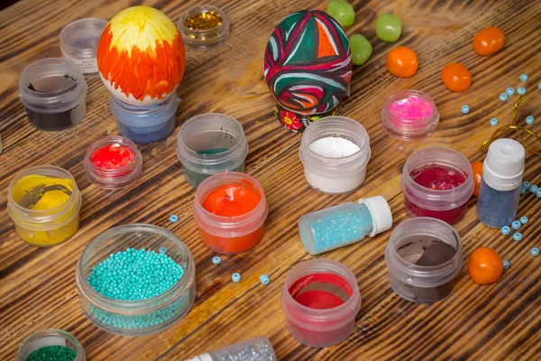 Cans of paint, glitters,  painted easter eggs, candies on wood — Stock Photo, Image