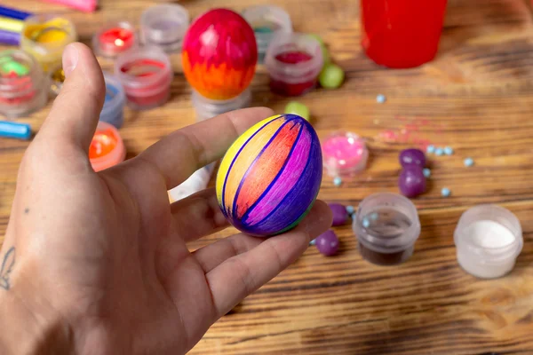 Holding painted easter egg in hand, celebrating prepatations, wooden table — Stock Photo, Image