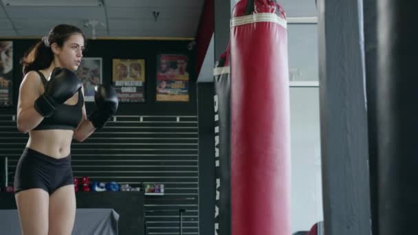 Boxe, mulher lutadora treina seus socos, bate um saco de perfuração, dia de treinamento no ginásio de boxe, corpo de ajuste de força, a menina bate rápido. — Vídeo de Stock