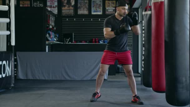 Caucasian handsome man wearing boxing gloves punching ahead on sandbag in gym or fitness club. — Stok video