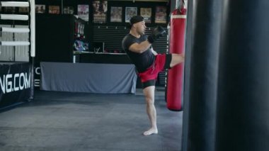Caucasian handsome man wearing boxing gloves punching ahead on sandbag in gym or fitness club.