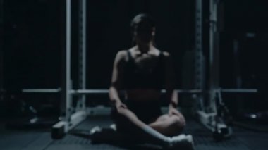 Sporty Caucasian woman sitting alone after workount in the dark gym.