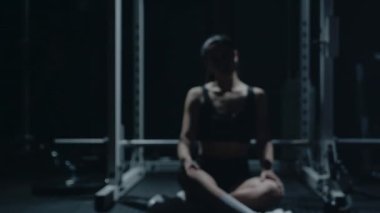 Sporty Caucasian woman sitting alone after workount in the dark gym.
