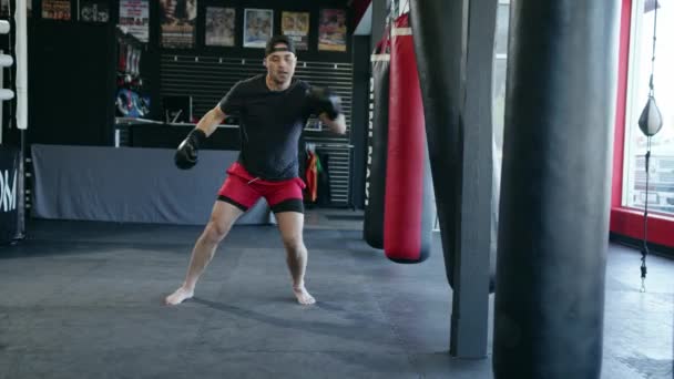 Caucasian handsome man wearing boxing gloves punching ahead on sandbag in gym or fitness club. — Stok video