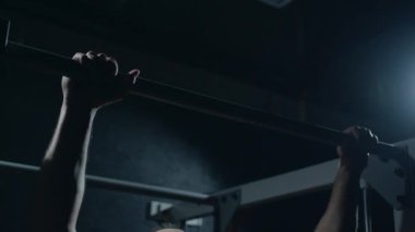 Young sportsman is doing a pull-up on the crossbar. Hard training of professional sportsman, dark background.