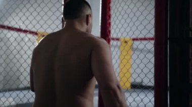 Muscular MMA fighter is entering the octagon cage and closing it.