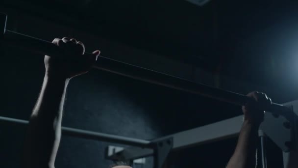 Young sportsman is doing a pull-up on the crossbar. Hard training of professional sportsman, dark background.