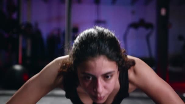 Young beautiful woman is doing push-ups on her knees in a gym, on black. — Stok video