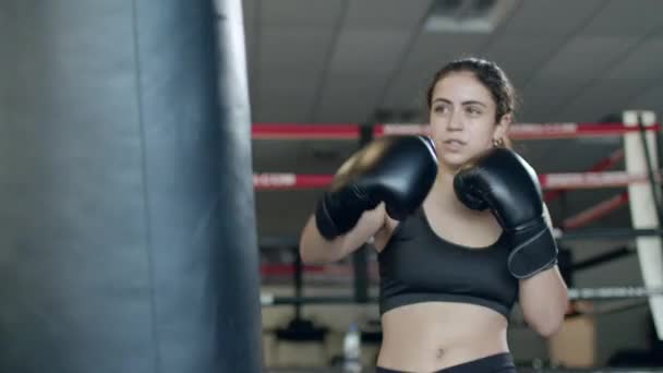 Boxeo, mujer luchadora entrena sus golpes, supera un saco de boxeo, día de entrenamiento en el gimnasio de boxeo, cuerpo de fuerza en forma, la chica golpea rápido. — Vídeos de Stock