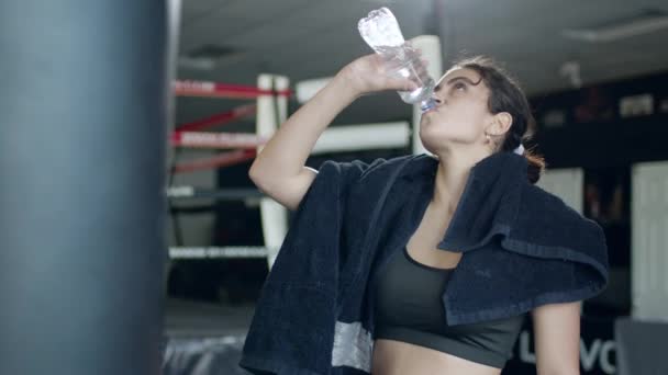 Odpowiednia kobieta w odzieży sportowej relaksująca się w siłowni i wodzie pitnej, sprzęt na tle. — Wideo stockowe
