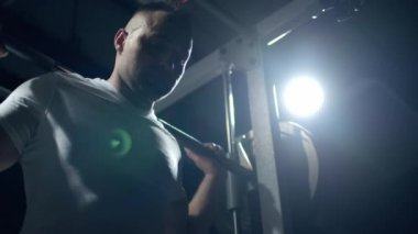 Young sportsman lifting heavy barbell. Hard training of professional sportsman, dark background.