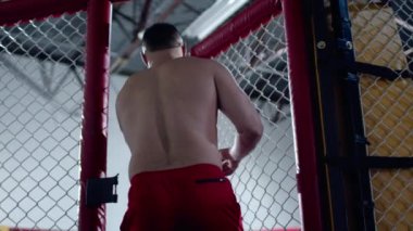 Muscular MMA fighter is entering the octagon cage and closing it.