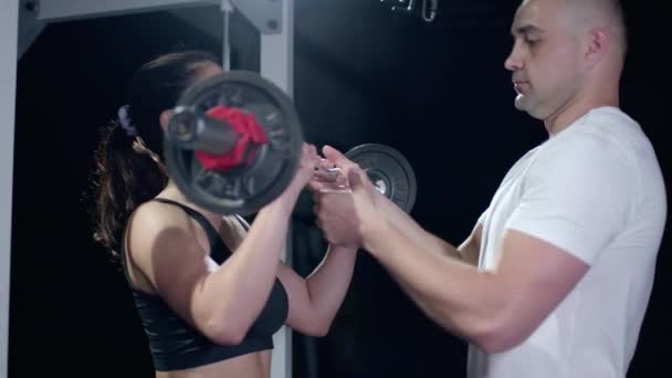 Ung tränare tittar på muskulös kvinna gör motion med viktad skivstång i cross training gym — Stockvideo