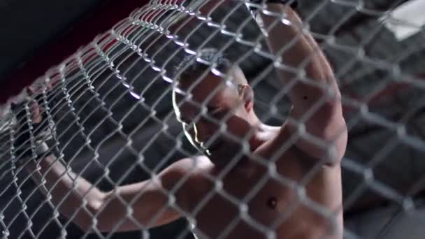 Muscular MMA fighter is hitting the octagon cage in anger. Fighter is holding on to the fencing of the cage. — Stock Video