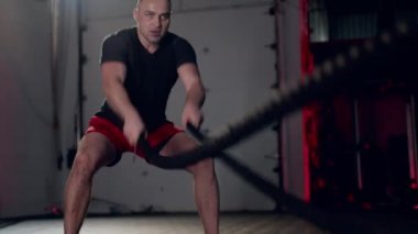 Assertive man doing exercises with battle rope, ruthlessly effective workout.