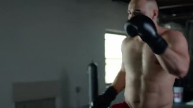 Caucasian handsome man wearing boxing gloves punching ahead on sandbag in the dark room.