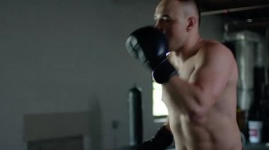 Caucasian handsome man wearing boxing gloves punching ahead on sandbag in the dark room.