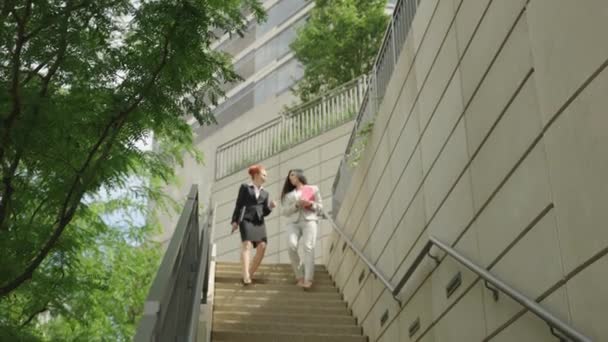 Duas mulheres bonitos elegantes em belos ternos de negócios estão andando pela cidade e conversando uns com os outros. — Vídeo de Stock