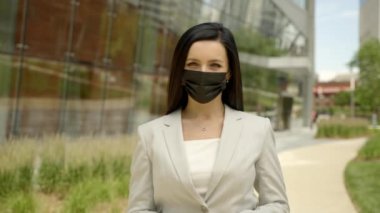 Cheerful brunette woman standing on street near modern office building and dropping off medical mask virus protection.