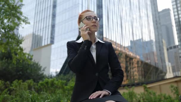 Joven mujer de negocios con el pelo rojo jengibre hablando en el teléfono móvil en la ciudad. — Vídeo de stock