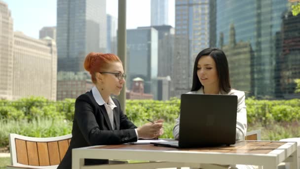 Close-up portrait of two beautiful concentrated business women talking at the table in outdoor restaurant. — Video