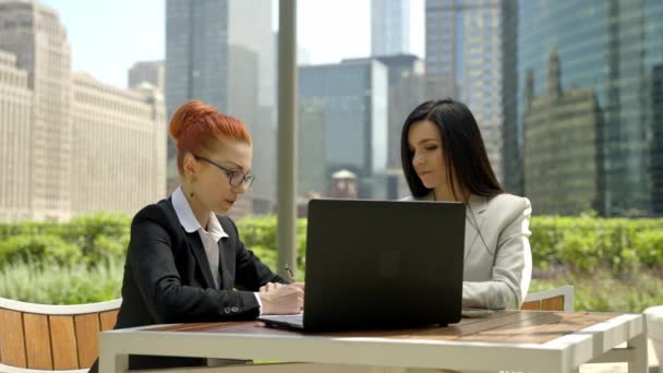 Close-up portrait of two beautiful concentrated business women talking at the table in outdoor restaurant. — Stok video