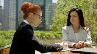 Close-up portrait of two beautiful concentrated business women talking at the table in outdoor restaurant.