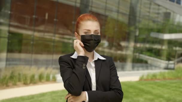 Cheerful red hair woman standing on street near modern office building and dropping off medical mask virus protection. — Video