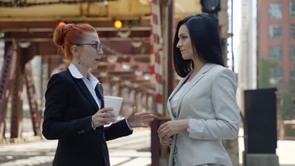Dos mujeres lindas con estilo en trajes de negocios hermosos están de pie alrededor de la ciudad y hablando entre sí. — Vídeos de Stock