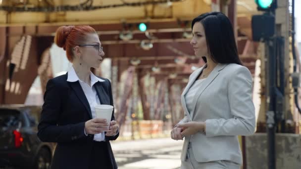 Two stylish cute women in beautiful business suits are standing around the city and talking to each other. — Video