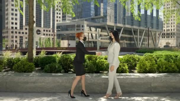 Twee jonge blanke vrouwelijke zakenvrouwen in het gezicht maskers naderen elkaar, het nemen van gezicht maskers af en schud de handen. — Stockvideo