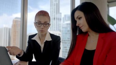 Two business woman working together in office with reports and laptop. Having a break, talking to each other.
