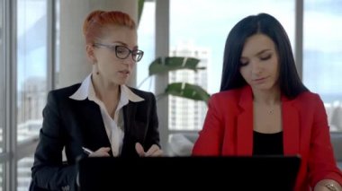 Two business woman working together in office with reports and laptop. Having a break, talking to each other.