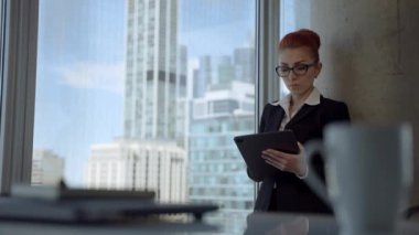 Beautiful young woman with red hair working in the office, using tablet computer device and coming up with idea.