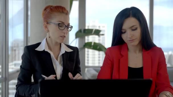 Duas mulheres de negócios trabalhando juntas no escritório com relatórios e laptop. A fazer uma pausa, a falar uns com os outros. — Vídeo de Stock