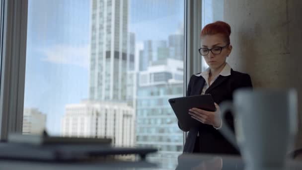 Beautiful young woman with red hair working in the office, using tablet computer device and coming up with idea. — Stock Video