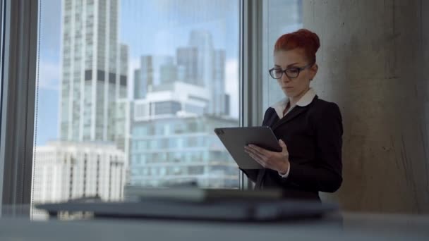 Hermosa mujer joven con el pelo rojo que trabaja en la oficina, el uso de un dispositivo de tableta y llegar a la idea. — Vídeos de Stock