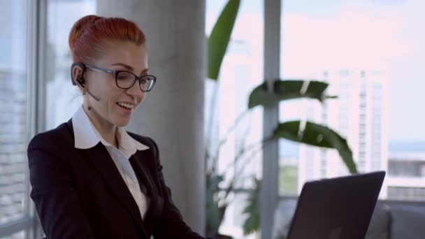 Lächelnde junge Geschäftsfrau an der Rezeption trägt drahtlose Kopfhörer-Videokonferenz am Laptop. — Stockvideo