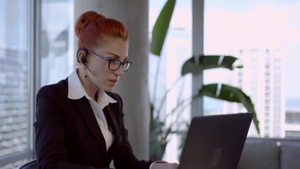Uśmiechnięta młoda kobieta biznesu recepcjonistka nosić bezprzewodowe słuchawki wideokonferencji pracy na laptopie. — Wideo stockowe