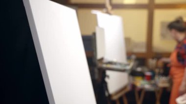 Boya ve fırçalarla resim yapmaya başlamak için sehpaya yaklaşan kadın sanatçılar.