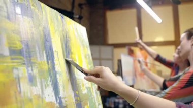 Kadın ressam yağlı boya ve boya kazıyıcı ile tuvale resim çiziyor. Yakın çekim..