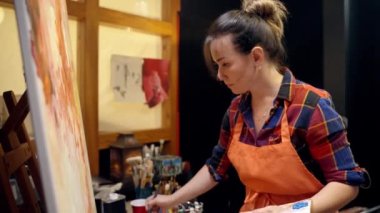 Kadın sanatçı fırçayla tuvale resim çiziyor. Tuvale soyut resim çiziliyor.