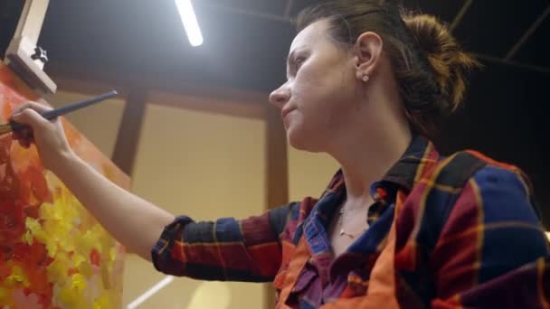 Woman artist is drawing on canvas with oil paint and soaking the brush in the paint. — Stockvideo